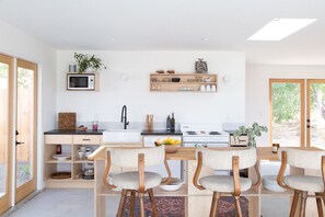 A modern kitchen with a central island, wooden chairs, and a dining table. - Minimalist desert retreat (Joshua Tree)
