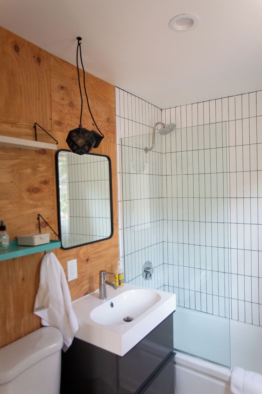 Un baño moderno con tocador de madera, un espejo grande, un lavamanos blanco y una zona de ducha con azulejos.