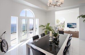 A modern dining area with a large table, chairs, and a view of the ocean.