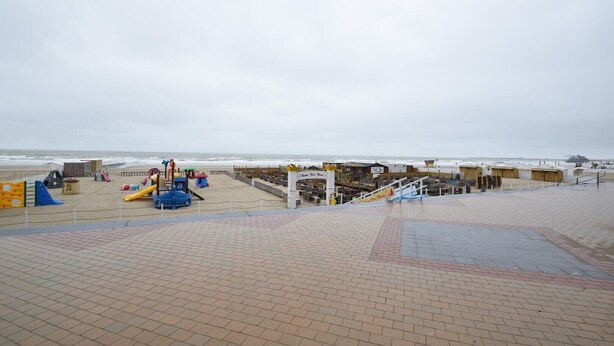 Een strandboulevard met een speeltuin, een houten constructie en een trap naar een strandgedeelte.