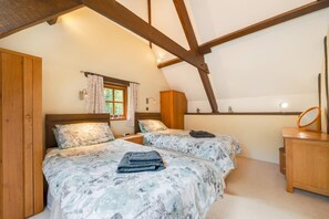 Un dormitorio con dos camas, armario de madera, una ventana con cortinas y un espejo sobre una cómoda.