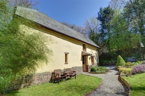 A rustic building with a stone wall and wooden furniture outside.