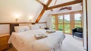 A bedroom with a large bed, wooden beams, a view of the outdoors, and a chair.