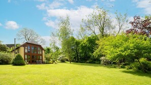 A two-story house with a well-maintained lawn and a variety of trees and shrubs.