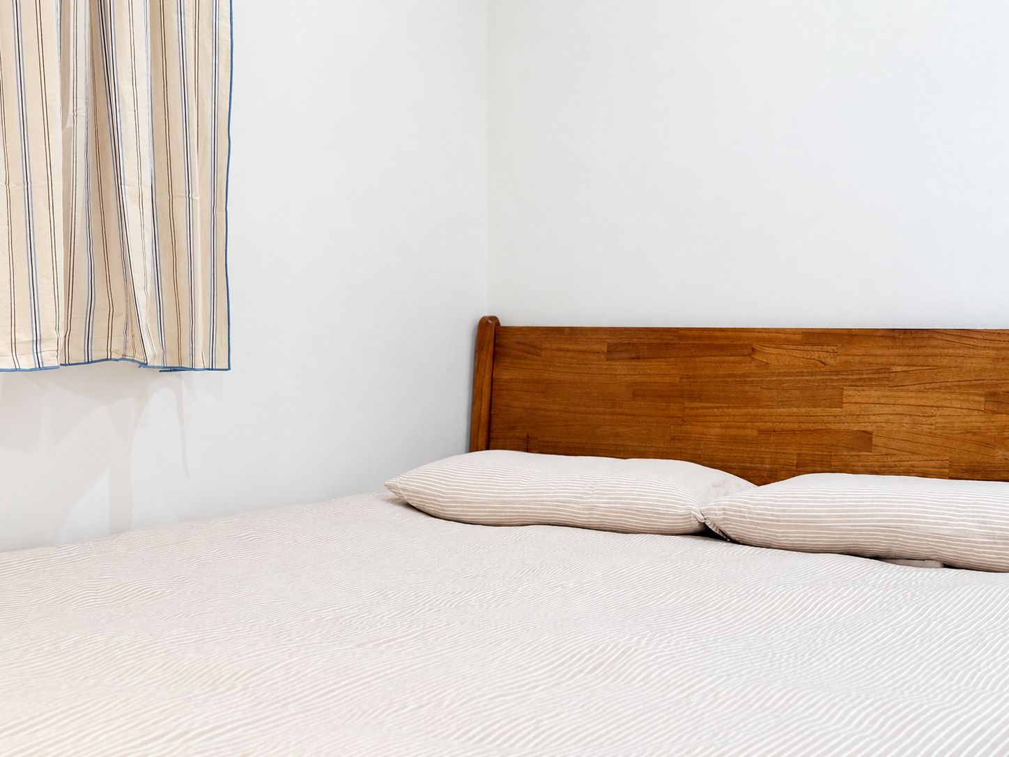 Un lit avec une tête de lit en bois, un rideau à rayures et une couvre-lit à motifs.