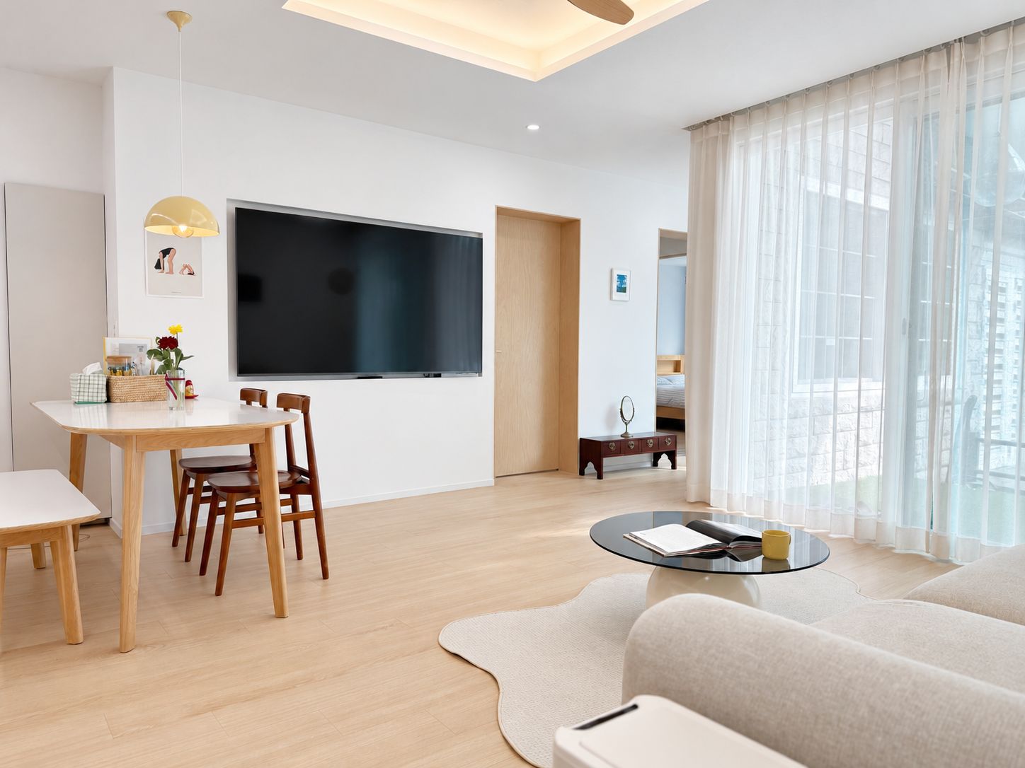 A modern living room with a flat-screen TV, a dining area with a table and chairs, a sofa, and a coffee table.