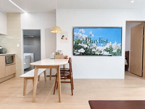 A modern kitchen with a dining area, a large wall-mounted TV, and a door leading to another room. - 6Min Hongdae | 83㎡ Family House | Private Yard (서울)