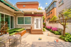 A residential building with a stone facade, a front porch with a bench, and a small garden area with pink flowers. - 6Min Hongdae | 83㎡ Family House | Private Yard (서울)