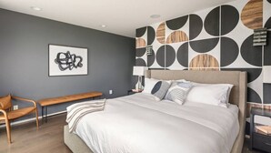 Une chambre moderne avec un grand lit, un banc et un mur orné d’un motif géométrique.