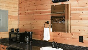 A compact wooden cabin-style bathroom with a sink, a coffee maker, a mirror, and a towel rack. - Beautiful Log cabin overlooking a meadow (Pipe Creek)
