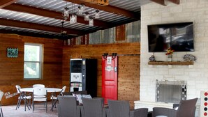 A rustic interior with exposed wooden beams, a brick fireplace, and a television mounted on the wall. - Beautiful Log cabin overlooking a meadow (Pipe Creek)