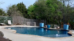 A swimming pool with a curved edge, surrounded by a concrete deck. There are lounge chairs and a wooden fence in the background. - Beautiful Log cabin overlooking a meadow (Pipe Creek)