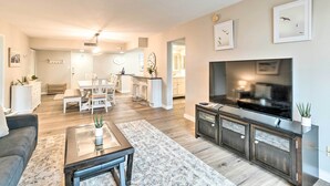 A modern living room with a flat-screen TV, a sofa, a coffee table, and a dining area in the background. - Walk to Beach: Resort-Style Siesta Key Condo! (Siesta Key)