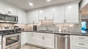 A modern kitchen with white cabinets, stainless steel appliances, and a tiled backsplash. - Walk to Beach: Resort-Style Siesta Key Condo! (Siesta Key)