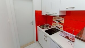 A compact kitchen with white cabinets, a stainless steel sink, and a red backsplash.