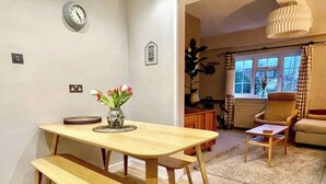 Un comedor con una mesa de madera y un banco, un jarrón con flores y un reloj en la pared.