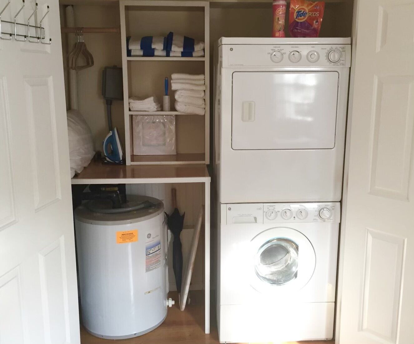 A compact laundry room with a front-loading washing machine and dryer, a small shelf with folded towels, and a water heater.