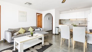 A modern living room with a grey sofa, a white coffee table, and a dining area with a wooden table and chairs. - 2-bedroom flat on Palm Mar beachfront with stunning view (Palm Mar)