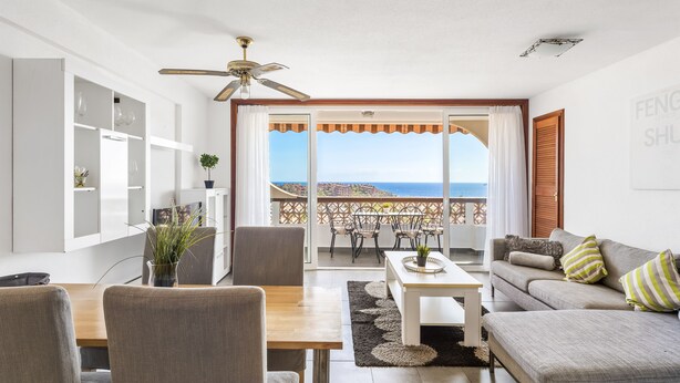 A living room with a sofa, dining table, chairs, and a balcony with a view of the sea. - 2-bedroom flat on Palm Mar beachfront with stunning view (Palm Mar)