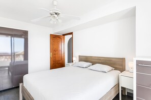 Quarto com cama, mesa de cabeceira, luminária, guarda-roupa e ventoinha no teto.