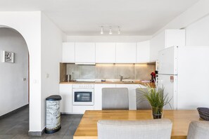 Una cocina moderna con armarios blancos, una mesa de comedor de madera y un cubo de basura.