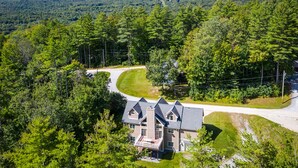 Une grande maison dotée d’une véranda qui fait le tour de la maison, entourée d’une forêt dense et bordée d’une route sinueuse.