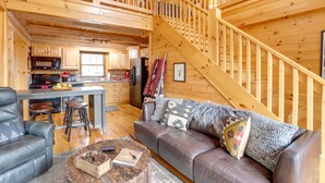 L’intérieur chaleureux d’un chalet avec un escalier en bois, un coin repas et un salon doté d’un canapé en cuir et d’une table basse.