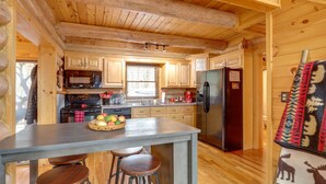 Une cuisine rustique aménagée dans une cabane en bois, avec un îlot central, des tabourets de bar, un réfrigérateur et un four à micro-ondes.