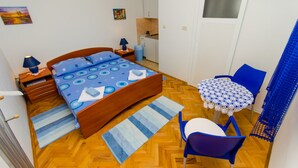 A compact bedroom with a bed, bedside tables, a small table with chairs, a kitchen area, and a window. - Apartments Ivana (TR) -Studio with Terrace ( A2) (Trogir)