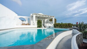 Ein moderner Poolbereich mit einem klaren blauen Pool, weißer Architektur und einer überdachten Sitzgelegenheit.