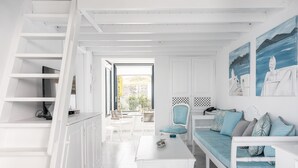 Ein helles, weißes Interieur mit Treppe, einer Couch mit gemusterten Kissen und Kunstwerken an den Wänden.