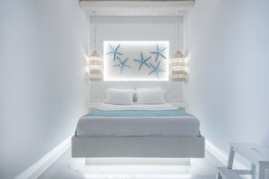 Un dormitori modern amb un llit blanc, una finestra gran i decoracions amb estrelles de mar.