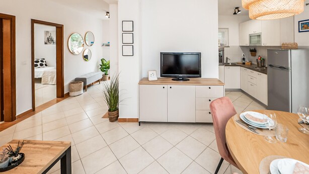 A modern kitchen with a TV, dining area with a table set for two, and a living area with a bench and plants. - 2 bedroom nice apartment in Rogoznica (Rogoznica)