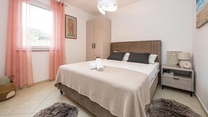 A bedroom with a bed, a nightstand, a lamp, a clock, a painting, and a window with curtains. - 2 bedroom nice apartment in Rogoznica (Rogoznica)