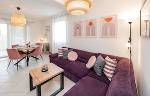 Una sala de estar moderna con un sofá morado, una mesa de centro de madera y un comedor con sillas rosas.