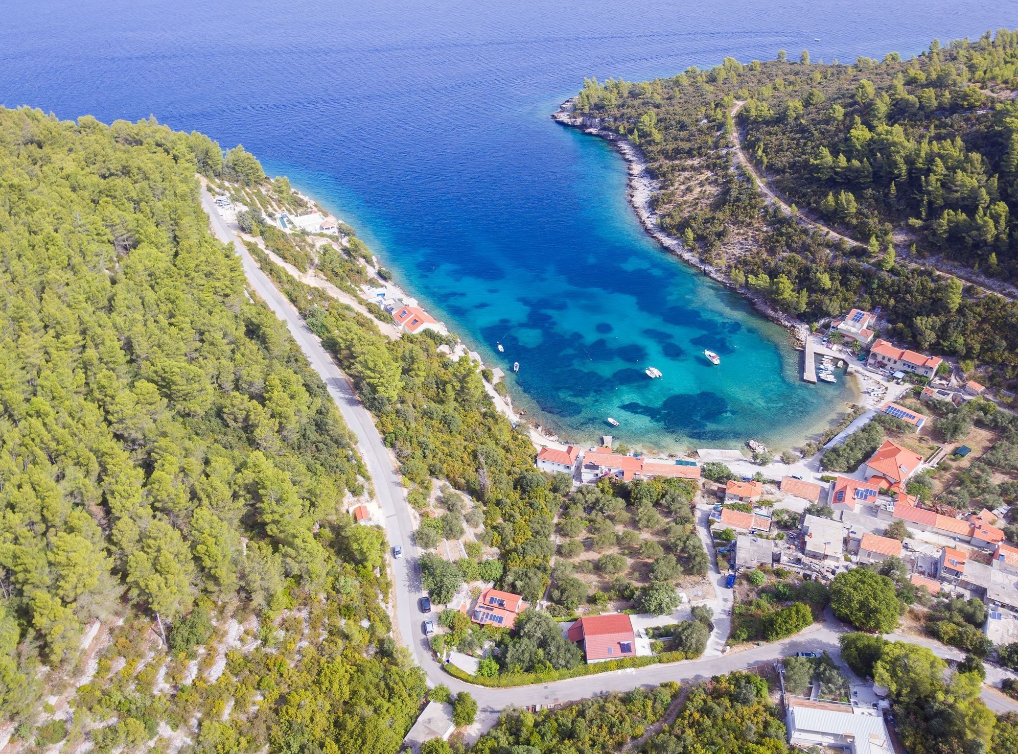 Vista aérea de uma área costeira com mar azul cristalino, uma estrada e edifícios com telhados vermelhos.
