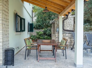 Eine überdachte Terrasse mit Holztisch und -stühlen, Steinmauern und Blumentöpfen.