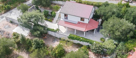 A two-story house with a red-tiled roof, surrounded by greenery and a paved driveway.
