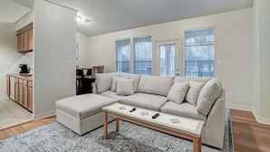 A living room with a sectional sofa, a coffee table, and a kitchen area with wooden cabinets. - Luxury vacation Kemah, TX condo. Bars and restaurants within walking distance. (Kemah)