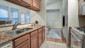 A kitchen with granite countertops, wooden cabinets, a stainless steel sink, a stove, and a window with blinds. - Luxury vacation Kemah, TX condo. Bars and restaurants within walking distance. (Kemah)