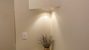 A corner of a room with a white wall, a small wooden shelf, and a potted plant. - Luxury vacation Kemah, TX condo. Bars and restaurants within walking distance. (Kemah)