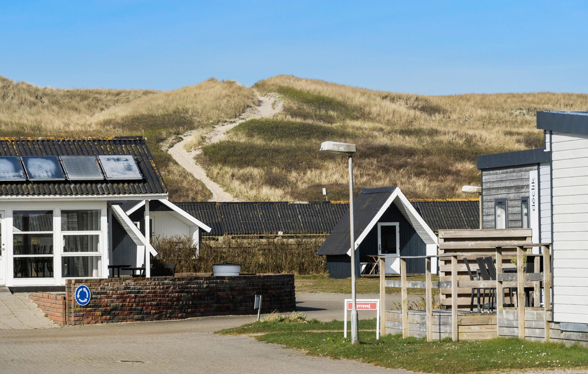 A coastal building with a sandy path leading to it, surrounded by dunes.