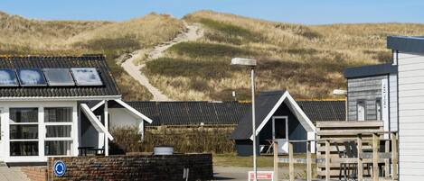 A coastal building with a sandy path leading to it, surrounded by dunes.