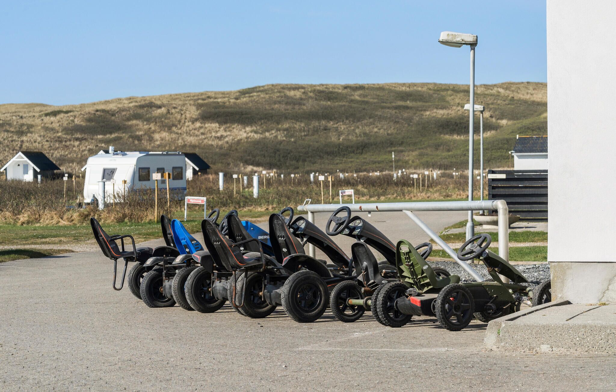 A row of ATVs parked on a paved area with a grassy hill and a white building in the background.