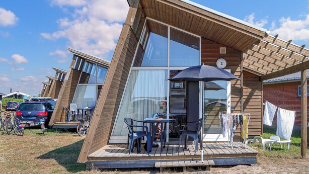 A modern, wooden cabin with a large glass door, a small patio with a table and chairs, and a number '2' sign on the door. - Beach front home in Hvide Sande (Hvide Sande)