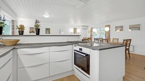 A modern kitchen with white cabinetry, a built-in oven, and a dining area with wooden chairs and a table. - Pet friendly home in Blåvand with sauna (Blåvand)
