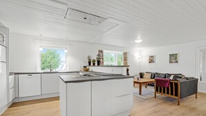 A modern kitchen with white cabinets, a central island, and a dining area with a sofa and table. - Pet friendly home in Blåvand with sauna (Blåvand)