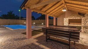 Un espace extérieur abrité comprenant une piscine, un sol en pierre, un banc en bois et une cheminée en pierre.