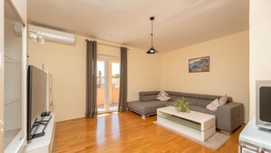 Un salon avec un canapé gris, une table basse blanche et un téléviseur à écran plat posé sur un meuble.