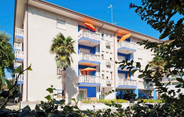 A multi-story building with balconies, a palm tree, and a clear blue sky.